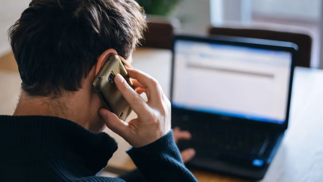 Personne contactant sa banque au téléphone devant son ordinateur