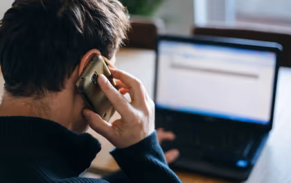 Personne contactant sa banque au téléphone devant son ordinateur